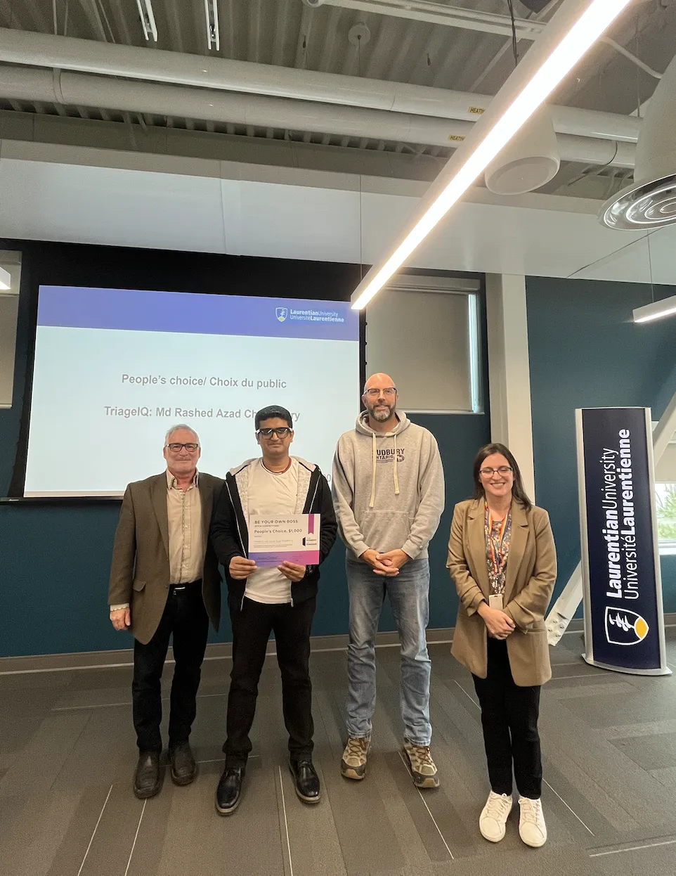 People's Choice BYOB winner Md Rashed Azad Chowdhury stands in the center of the stage holding his award certificate.