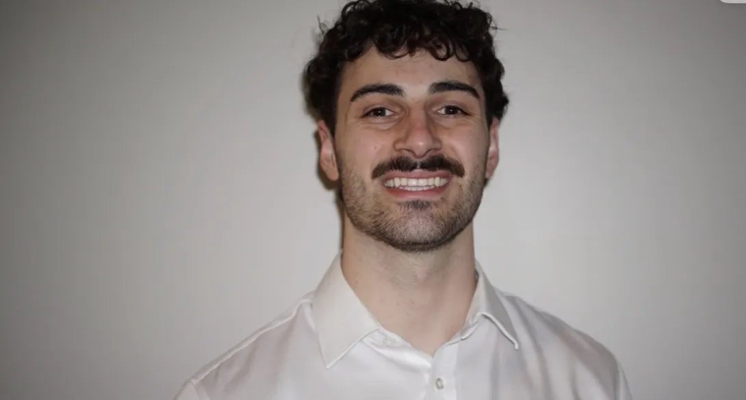 A formal close-up headshot of Evan Boudreau-Munro smiling warmly against a plain, neutral background. 