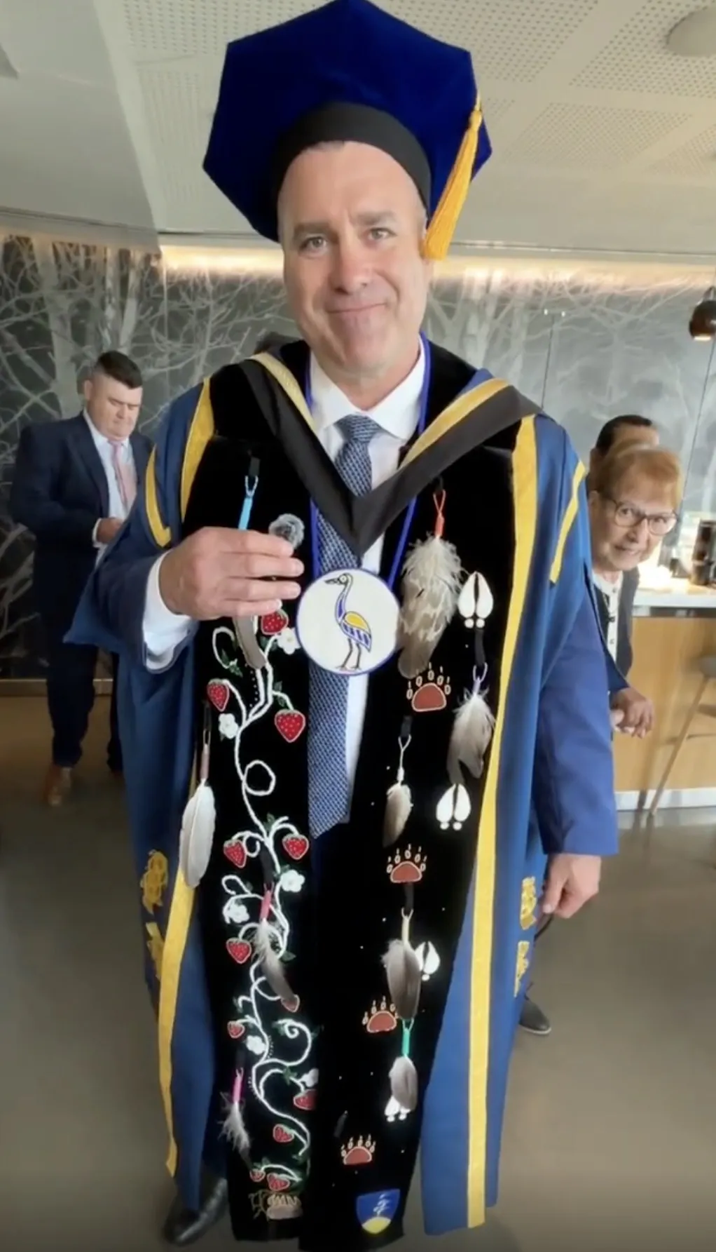 A portrait of Laurentian University Chancellor Kristan Straub, a member of Henvey Inlet First Nation, smiling and wearing his official academic robes and the custom Ajijaak Doodem (Crane Clan) chancellor's medallion.