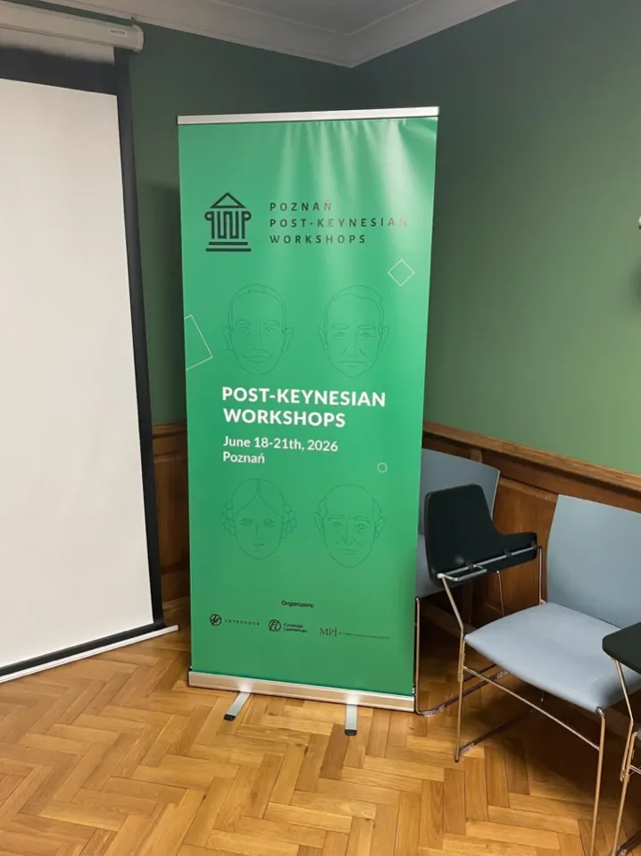 A tall, green promotional banner for the Poznań Post-Keynesian Workshops, dated June 18-21st, 2026, in Poznań, Poland. The banner features line-art illustrations of historic economists and stands in a classroom setting next to blue chairs and a projector screen.