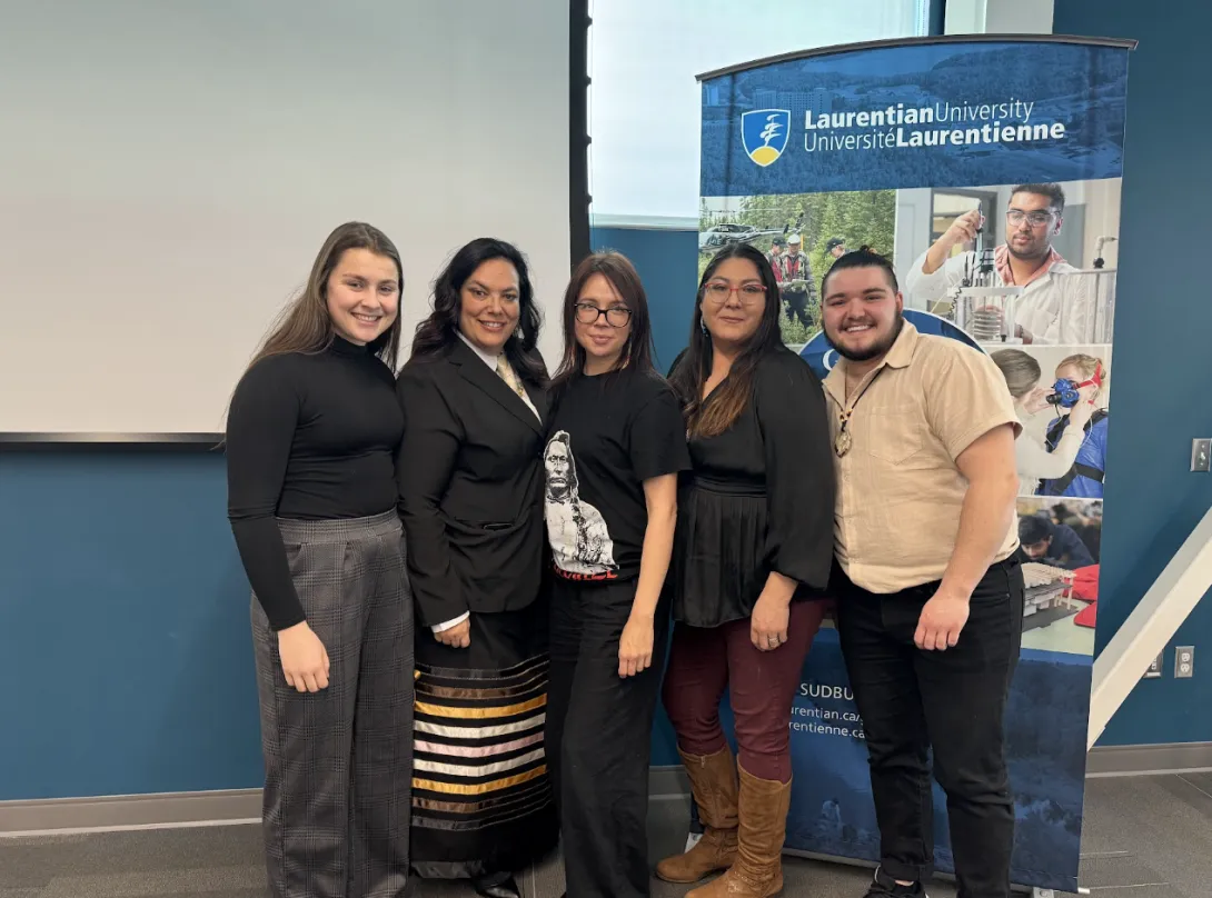 Connor Lafortune posing for a group photo with Laurentian University campus members in front of a university banner.