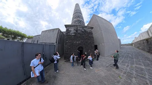 Architecture students explore a stone courtyard beside a tall chimney and concrete buildings at Arquipélago – Contemporary Arts Centre.