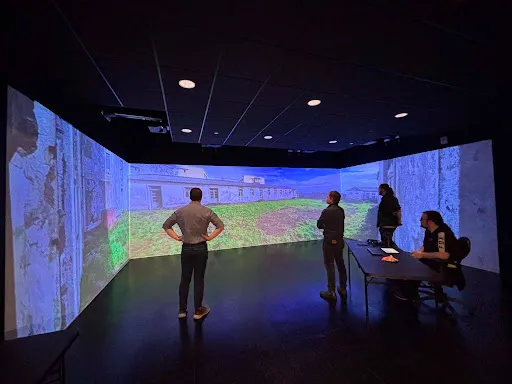 Four people view an immersive projection of the SINAGA factory site across three walls in Laurentian University’s virtual reality lab.