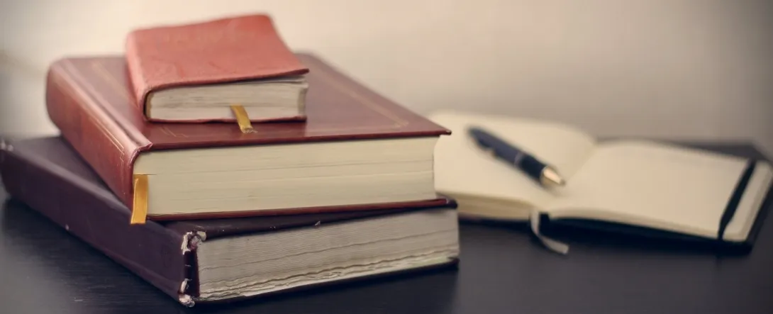 Une pile de livres et un cahier ouvert sur un bureau.
