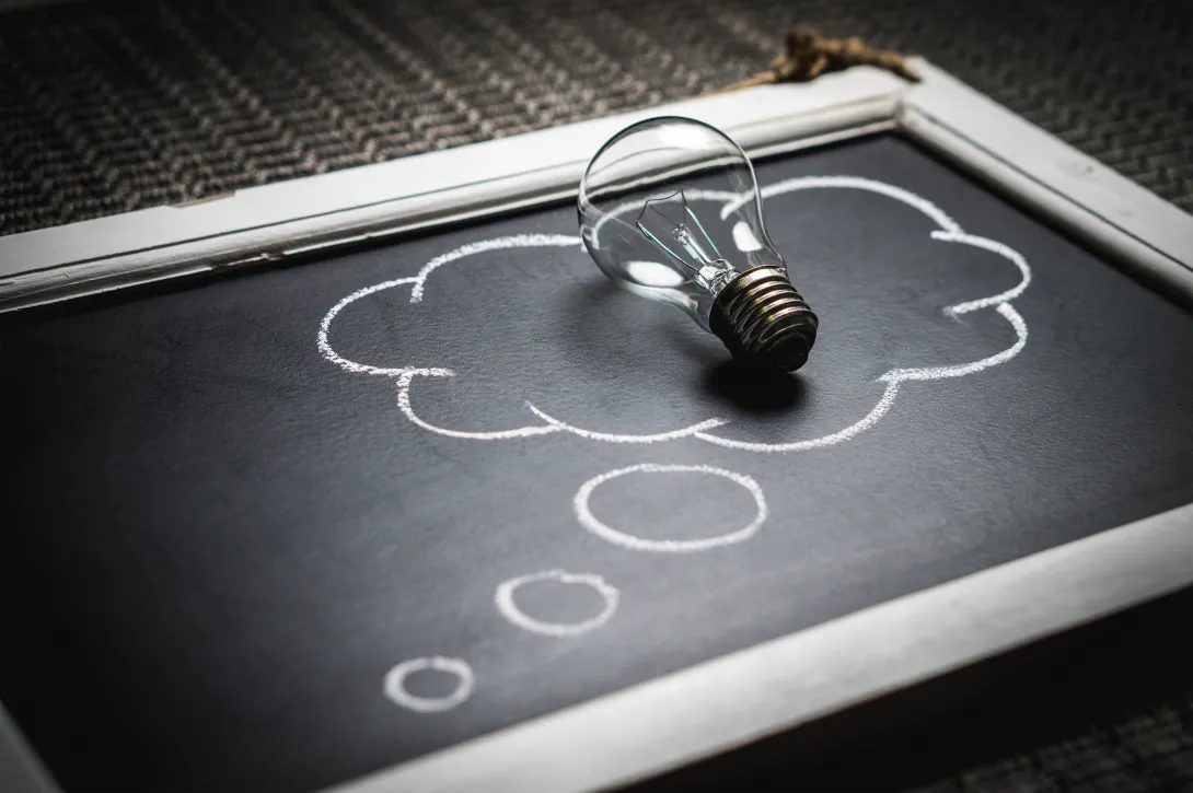 A chalkboard with a thought bubble drawing on it and a lightbulb